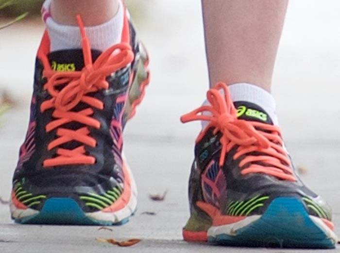 A close-up reveals Anne Hathaway&rsquo;s colorful Asics Gel-Kinsei trainers, with bright coral laces and cushioned soles designed for stability and long-distance comfort on the trail