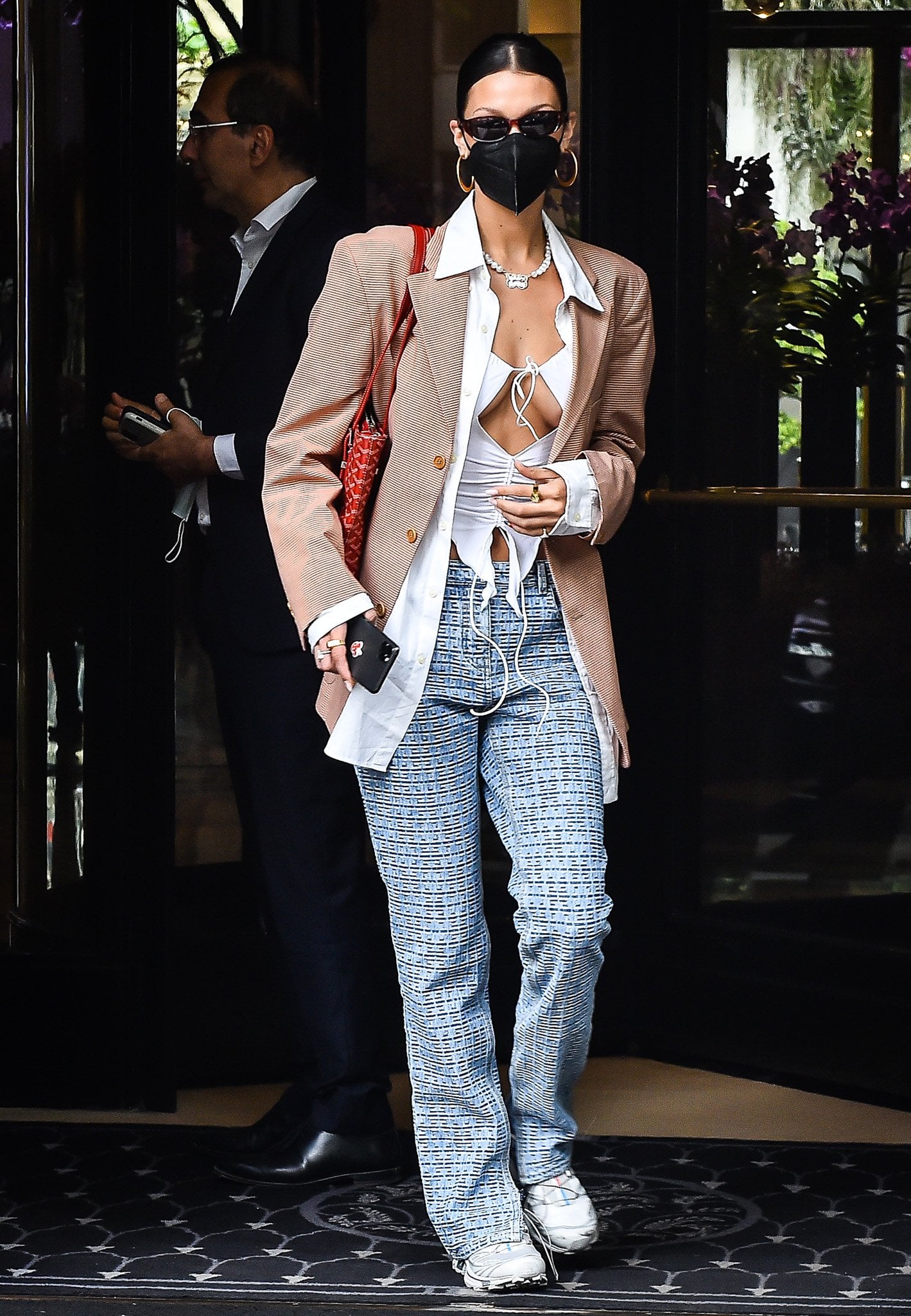 Bella Hadid styled her revealing I.Am.Gia Svana top with layered tailoring, wide-leg Givenchy monogram trousers, and sporty white Salomon sneakers for a sharp mix of Y2K streetwear and Paris Fashion Week off-duty dressing