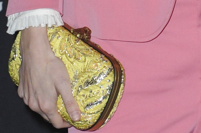 A close-up highlights Marling&rsquo;s gold embroidered clutch, its ornate texture adding contrast and warmth to her pastel pink tailoring