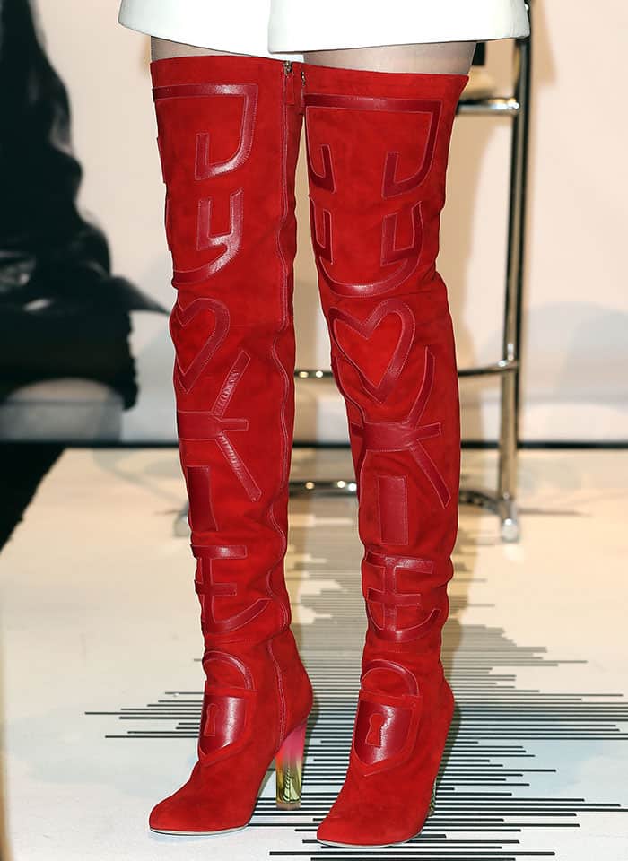 The Schiaparelli thigh-high boots feature suede construction with appliqu&eacute;d lettering and a sculptural silhouette that extends well above the knee