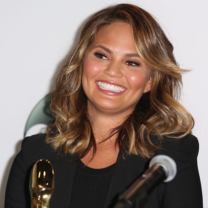 Chrissy Teigen flashes a radiant smile during the Billboard Music Awards Finalists Press Conference on April 7, 2015, wearing a sleek black blazer and softly waved, honey-highlighted hair