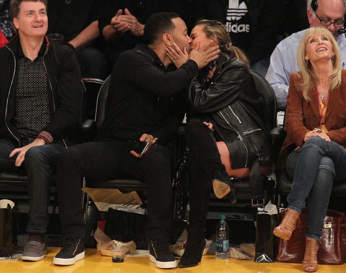 John Legend and Chrissy Teigen share a kiss for the kiss cam at a Los Angeles Lakers game, with Teigen wearing Chlo&eacute; suede and textured-leather over-the-knee boots styled with an Acne leather jacket