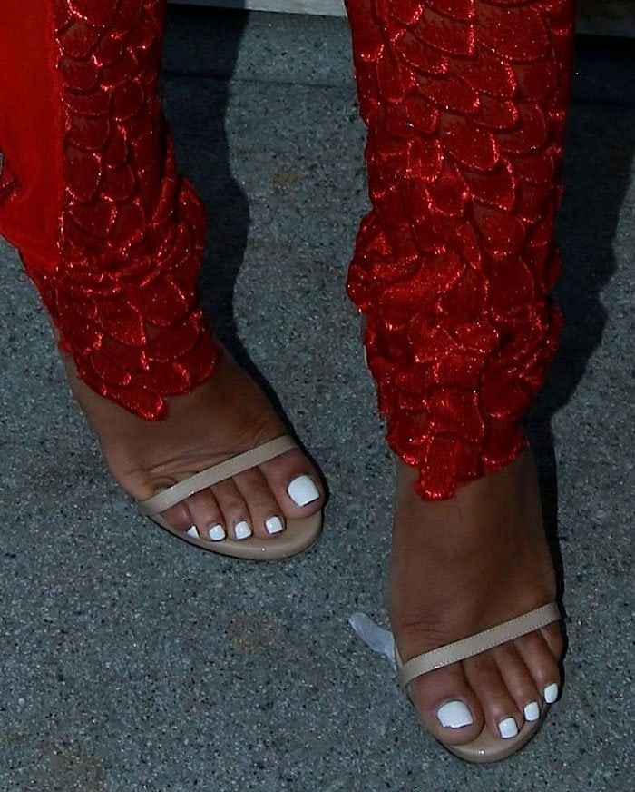 Christina Milian shows off her white pedicure in nude Stuart Weitzman &ldquo;Nudistsong&rdquo; sandals, adding a subtle contrast to her bold red lace trousers