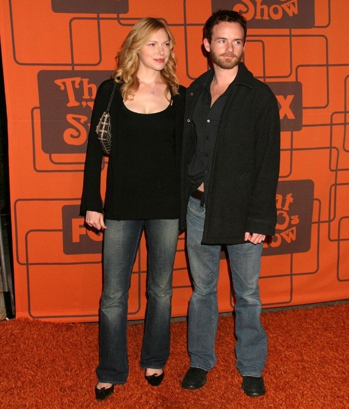 Laura Prepon, in a black top, flared jeans, and open-toe heels, poses with then-boyfriend Christopher Masterson at a That '70s Show event&mdash;highlighting their casual couple style during their relationship from 1999 to 2007