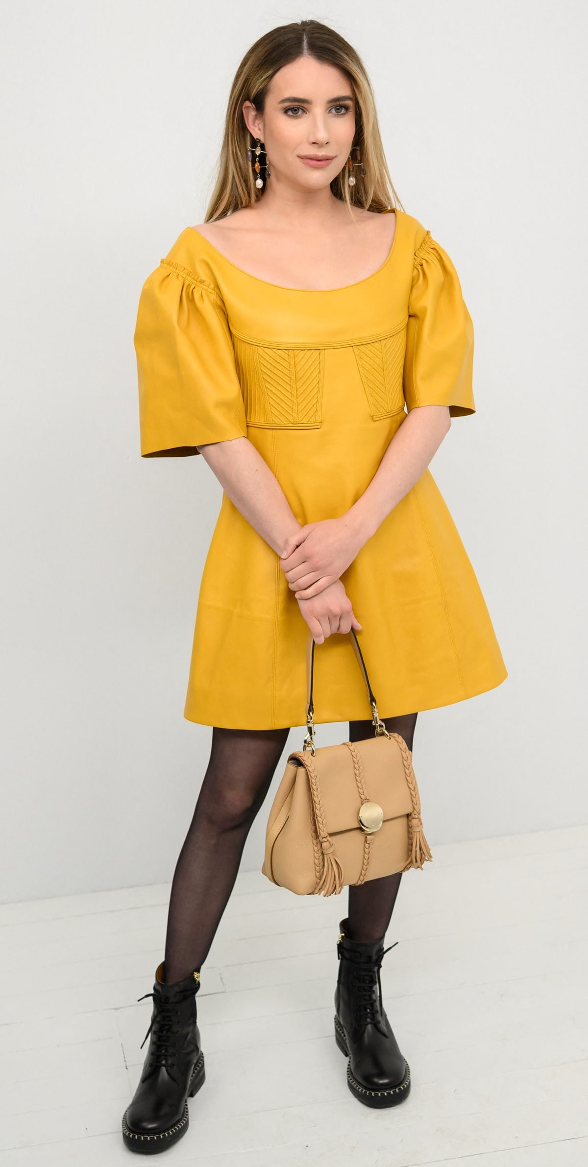 Emma Roberts attended Chlo&eacute;'s fall 2023 show on March 2, 2023, during Paris Fashion Week, dressed in a golden yellow leather mini dress, sheer black tights, lace-up boots, and accessorized with Chlo&eacute;'s multicolored stone and pearl drop earrings and a light tan Penelope leather satchel