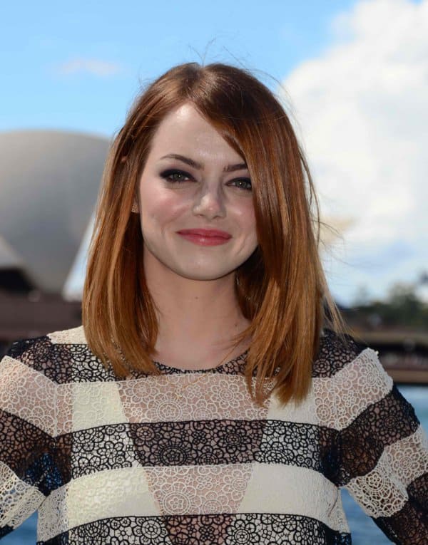 Emma Stone looks stunning in a dramatic black Lanvin PVC dress with a cinched waist and pockets, perfectly complemented by chic bow pumps