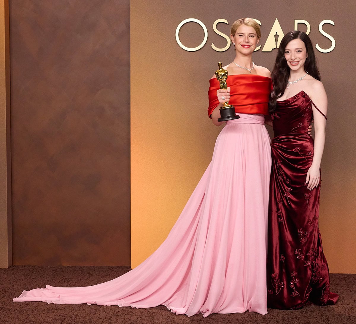 Jessie Buckley poses with her Oscar for Actress in a Leading Role beside Mikey Madison, who stuns in a rich red velvet Dior gown with floral appliqu&eacute;s, a thigh-high slit, and delicate beaded off-the-shoulder straps, styled with Tiffany & Co. jewelry and glossy Old Hollywood waves