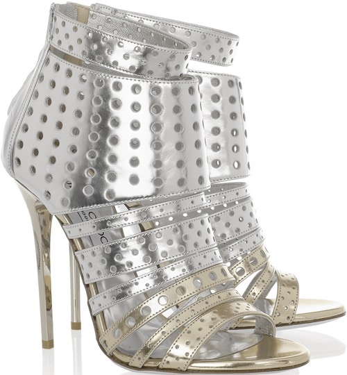 The silver Jimmy Choo &ldquo;Malika&rdquo; booties feature a high-shine metallic finish with dense perforation and layered straps that give the silhouette a bold, futuristic edge
