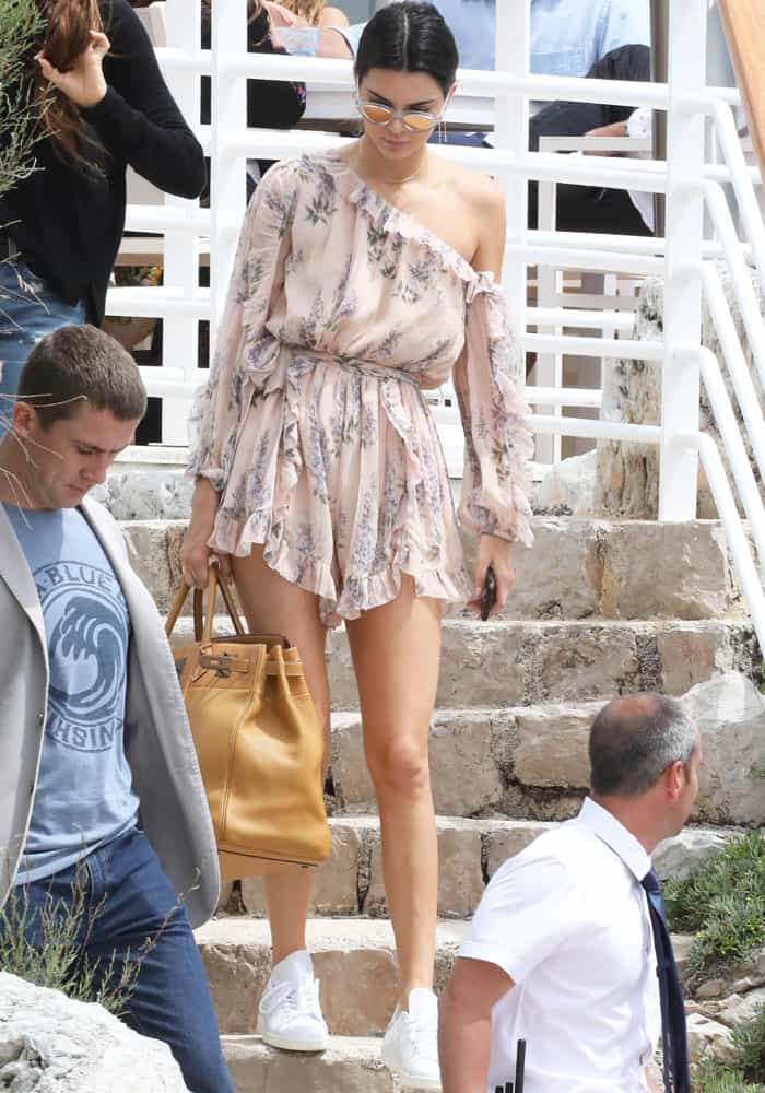 Kendall Jenner descends the steps in Cannes, effortlessly stylish in a floral Zimmermann romper, white Adidas 'Stan Smith' sneakers, and an oversized Herm&egrave;s Birkin bag
