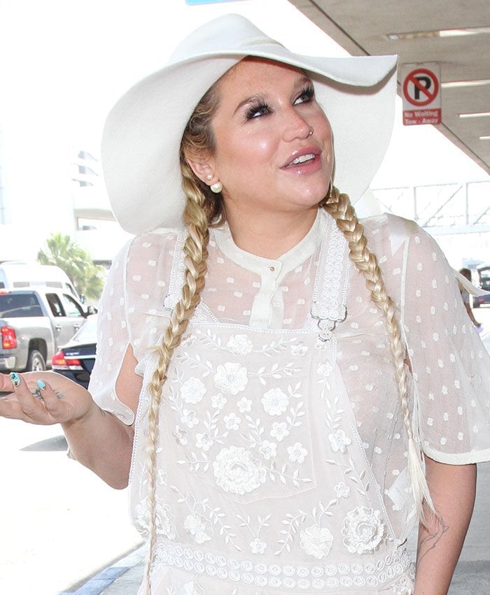 Kesha channels boho-chic vibes in a sheer embroidered white outfit, complete with a floppy hat and braided pigtails, while spotted at Los Angeles International Airport