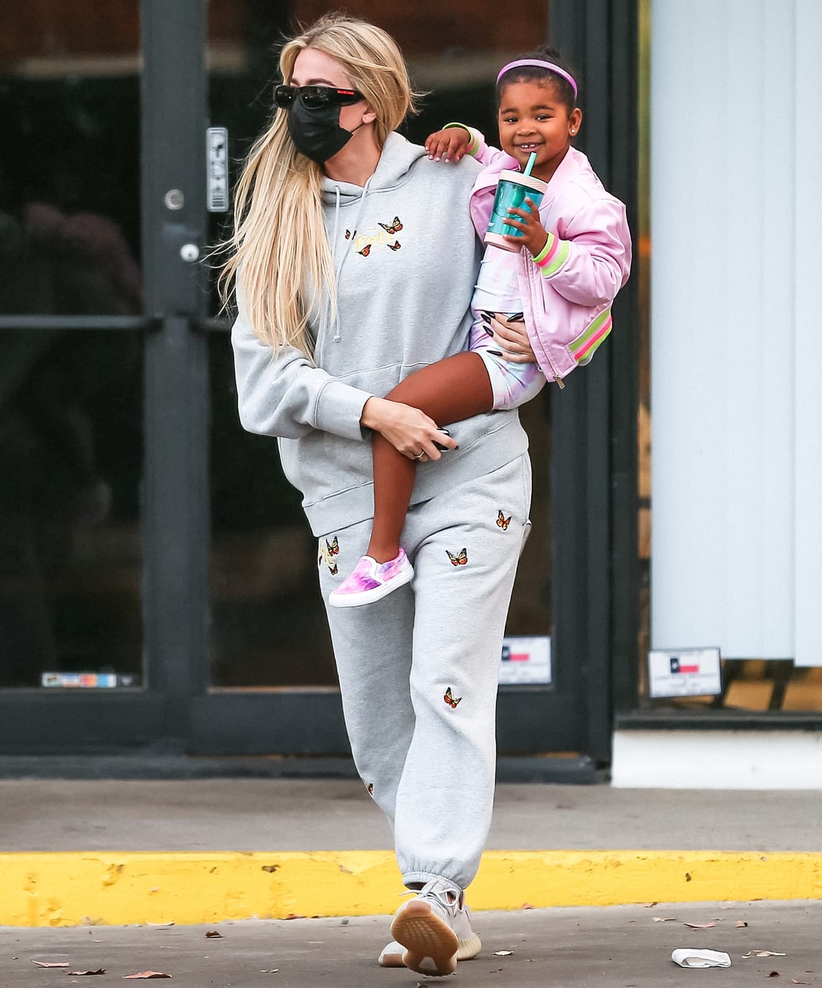 Wearing butterfly-embroidered sweatpants and a matching pullover hoodie by U.S streetwear company FELT, Khlo&eacute; Kardashian carries her tall daughter True Thompson