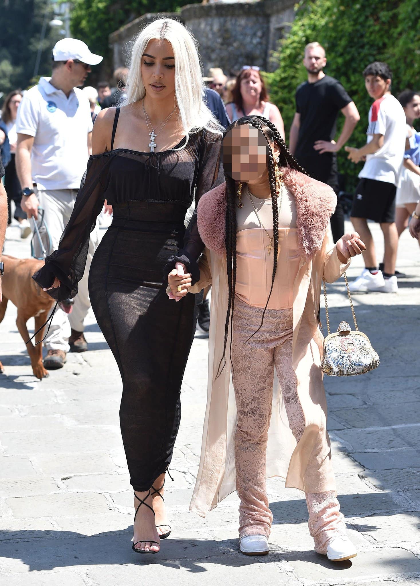Kim Kardashian walks through Portofino in a sheer black Dolce & Gabbana dress paired with delicate black crisscross-strap stiletto sandals while holding hands with daughter North West during the wedding festivities