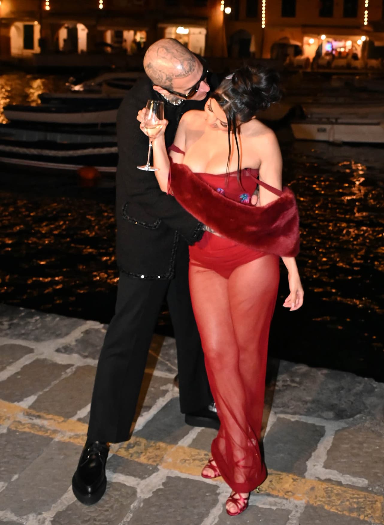 Kourtney Kardashian turns heads in a sheer red Dolce & Gabbana Spring 1998 dress paired with jeweled satin rose-heel sandals as Travis Barker embraces her during their pre-wedding dinner at Ristorante Puny in Portofino on May 20, 2022