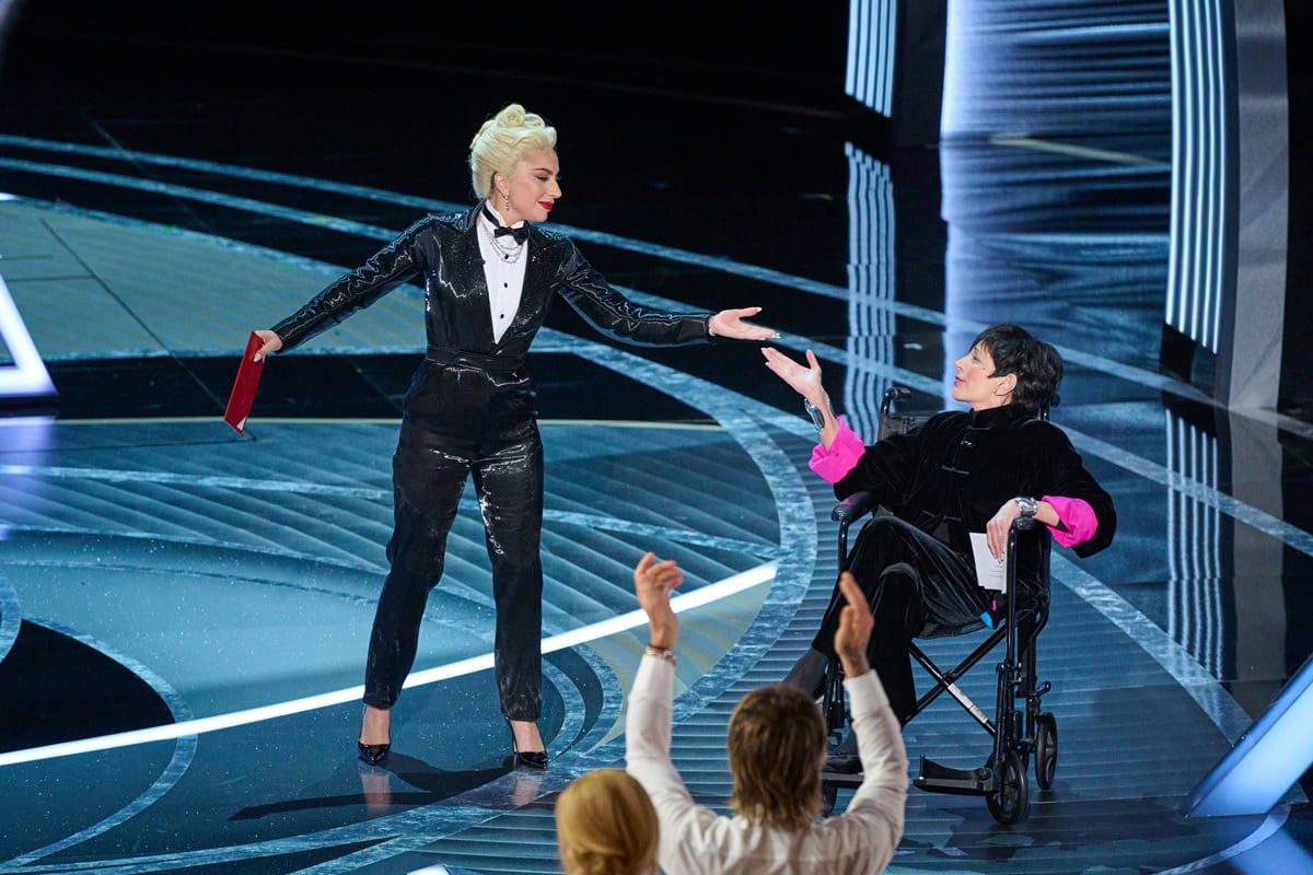 Lady Gaga joins Liza Minnelli onstage at the Oscars to present Best Picture, wearing a Ralph Lauren liquid lam&eacute; tuxedo jumpsuit with Jimmy Choo Romy heels and Tiffany & Co. diamond jewelry