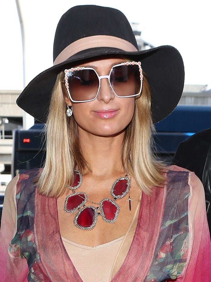 Paris Hilton over-accessorized with a black, wide-brimmed hat, Fendi "White Can Eye" embellished sunglasses, and a massive&nbsp;Kendra Scott "Ava" pink agate necklace