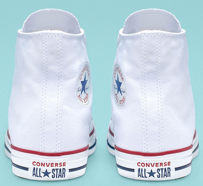 Authentic white Converse Chuck Taylor All Star sneakers featuring the signature rubber heel patch with red and navy branding