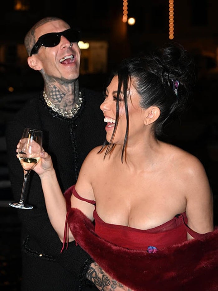 Kourtney Kardashian laughs with Travis Barker while wearing a sheer red Dolce & Gabbana Spring 1998 dress layered over a bodysuit and styled with a matching fur stole during their pre-wedding dinner celebration in Portofino