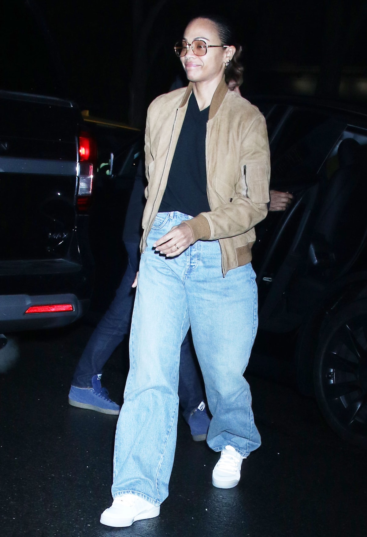 Zoe Salda&ntilde;a dresses casually in a black tee, baggy jeans, white sneakers, and a camel bomber jacket as she arrives at her Greenwich hotel on March 27, 2024
