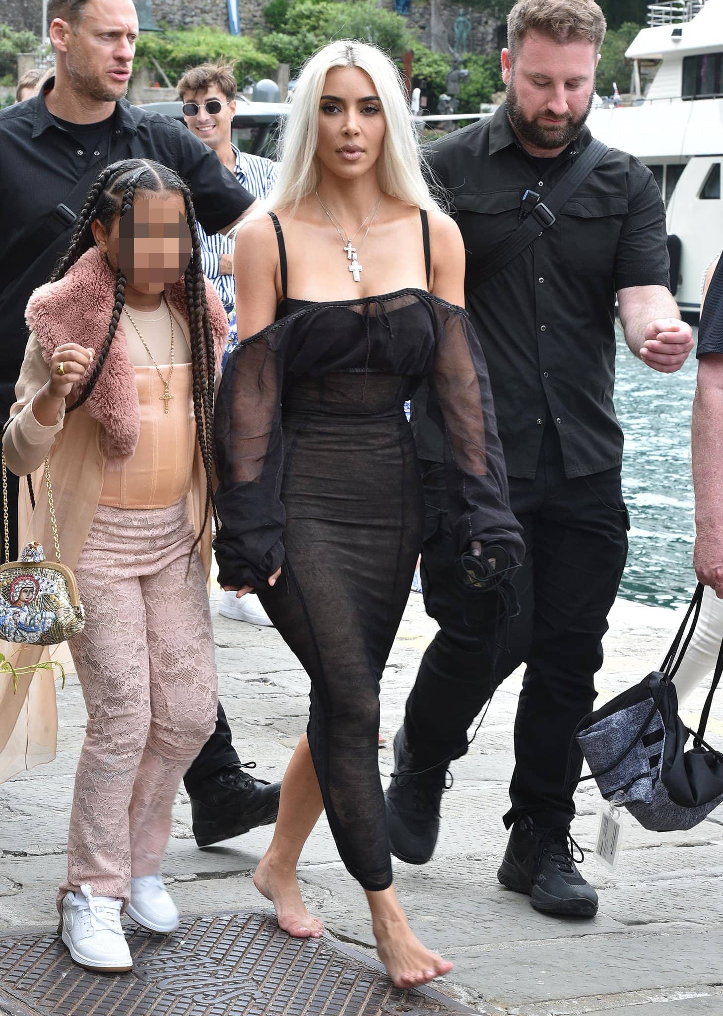 Kim Kardashian goes barefoot while walking through Portofino in a sheer black Dolce & Gabbana dress, carrying her heels as she holds hands with daughter North West